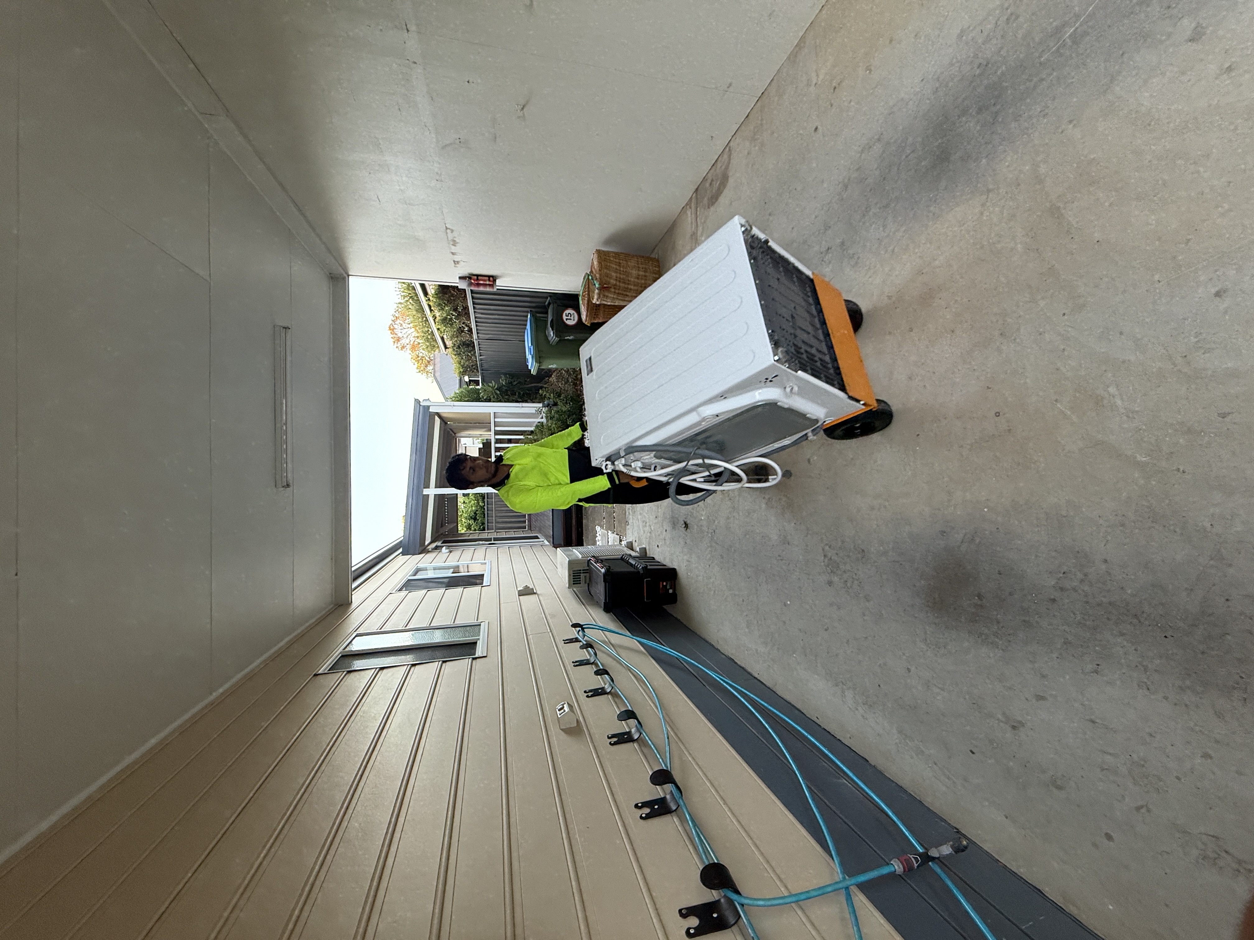 Mover rolling washing machine on trolley through narrow passage