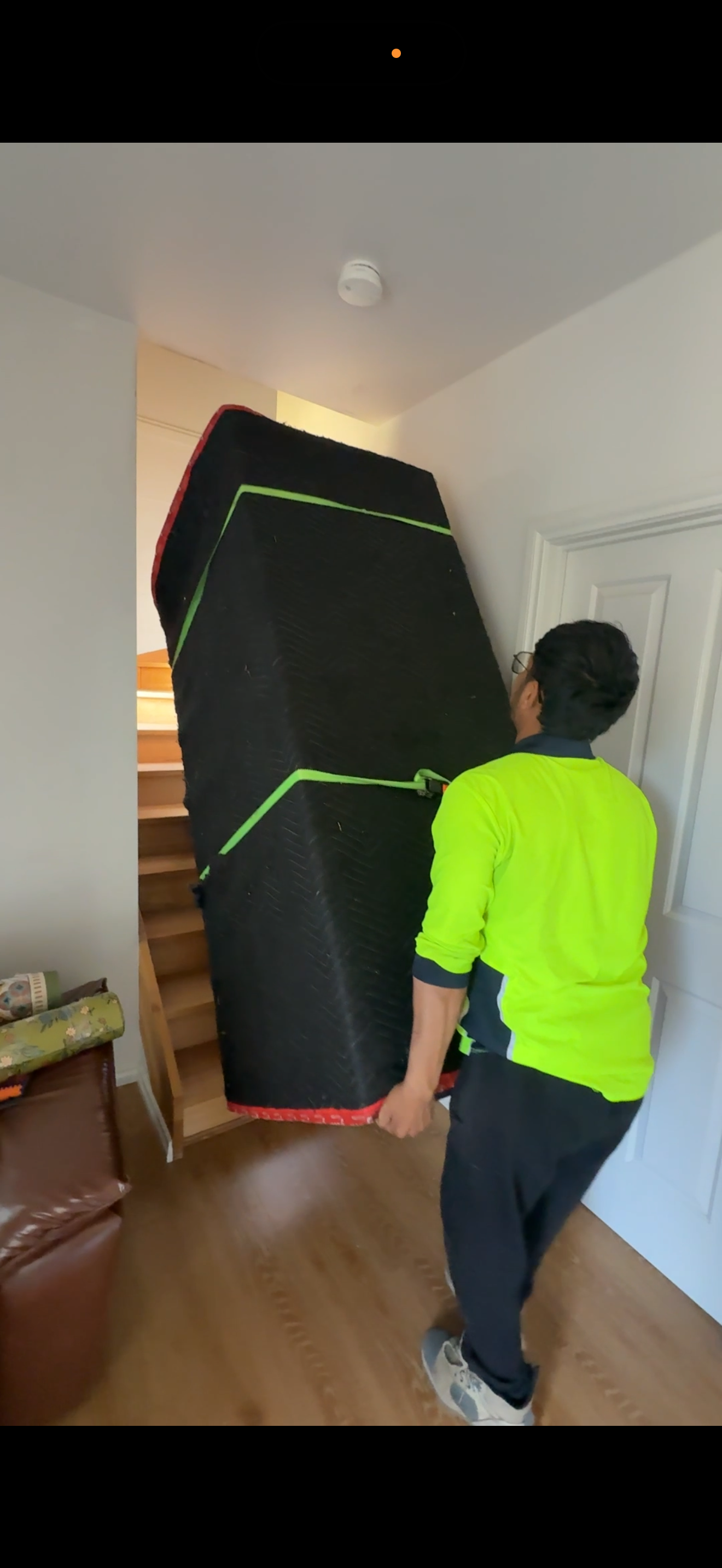 Mover in hi-vis carrying wrapped mattress up a tight staircase
